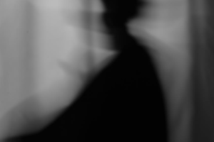 Abstract black-and-white silhouette of a person with motion blur against a curtain background.