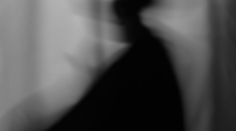 Abstract black-and-white silhouette of a person with motion blur against a curtain background.