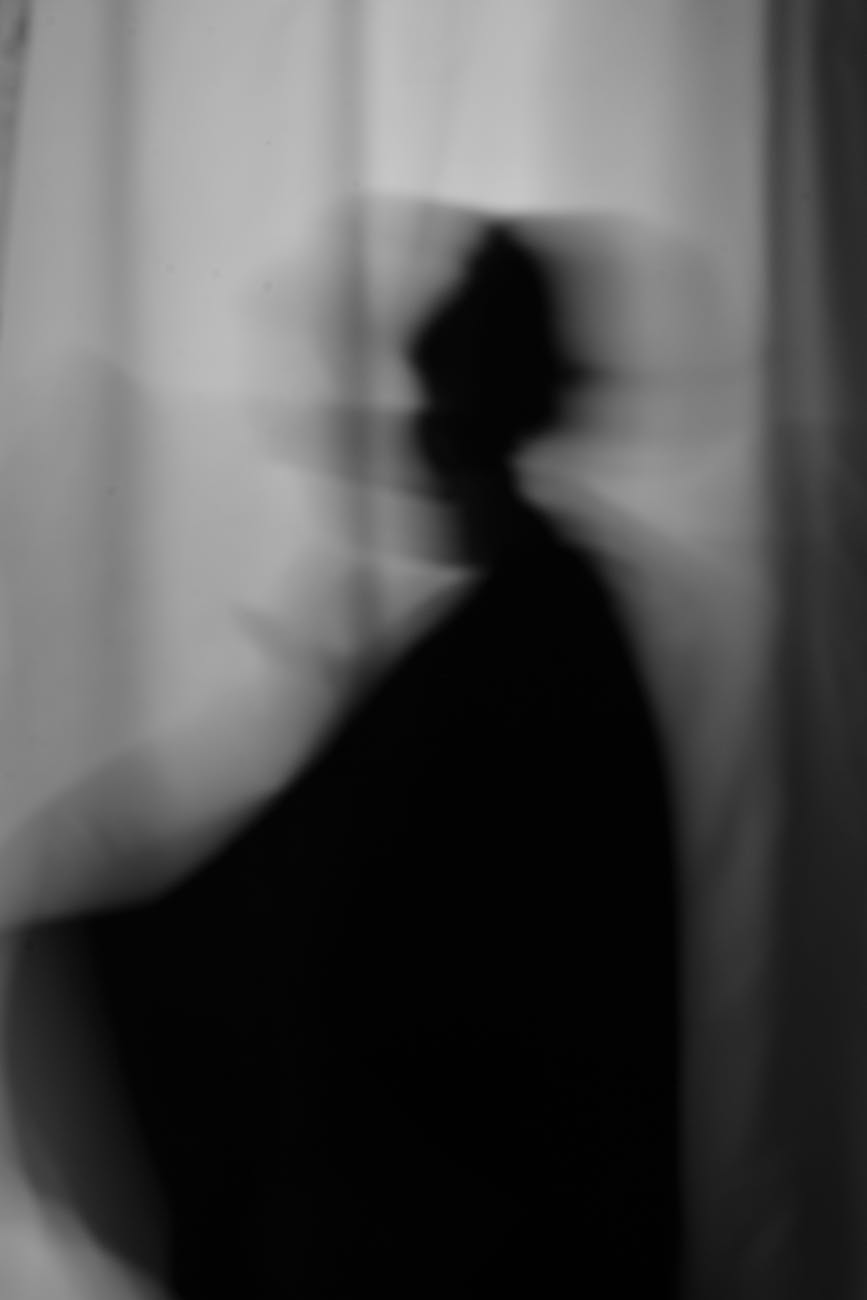 Abstract black-and-white silhouette of a person with motion blur against a curtain background.