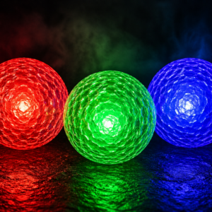 Three glowing golf balls in red, green, and blue on a dark reflective surface.