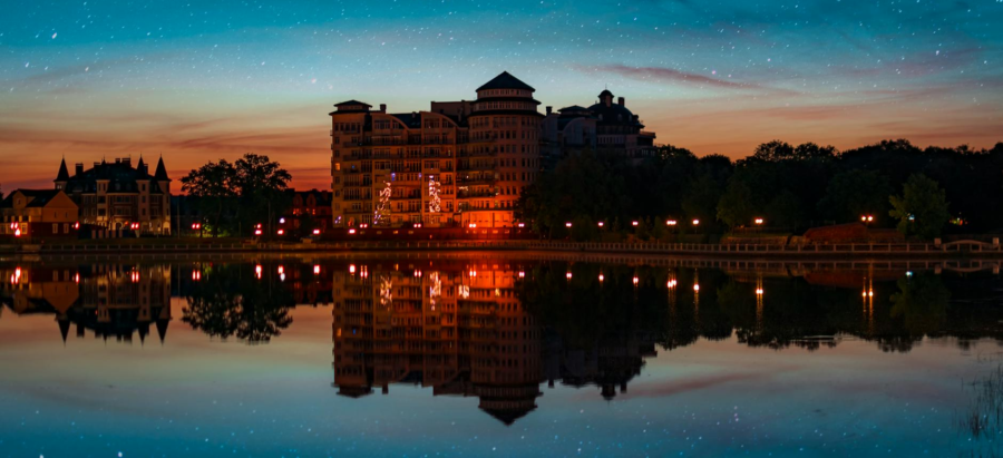Nighttime city skyline with illuminated buildings reflected in calm water under a starry sky