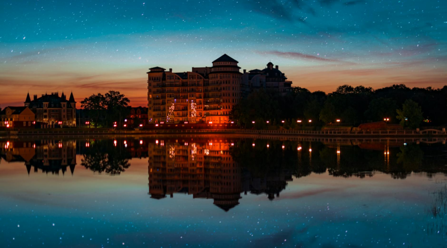 Nighttime city skyline with illuminated buildings reflected in calm water under a starry sky