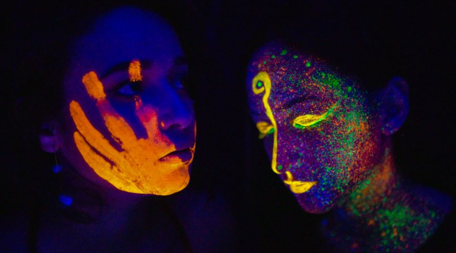 Two people with neon UV face paint glowing in the dark