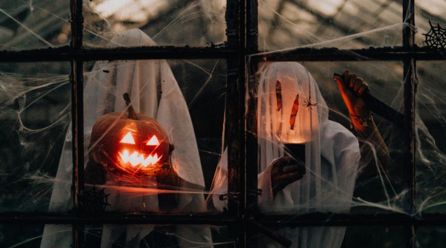 Glowing jack-o'-lantern and ghost decorations behind a window on Halloween