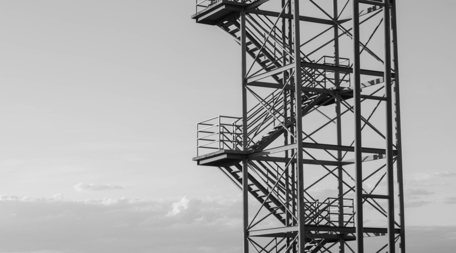 Black and white industrial observation tower with metal stairs against a cloudy sky