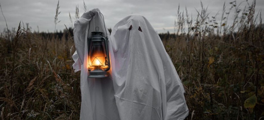 Two people dressed as ghosts hold a lantern in a dark field at night.
