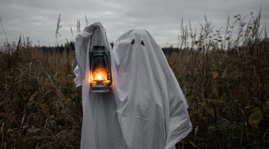 Two people dressed as ghosts hold a lantern in a dark field at night.