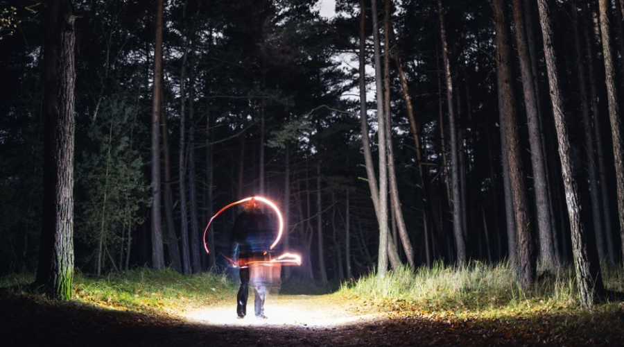 Person drawing light trails with a sparkler in a dark forest at night