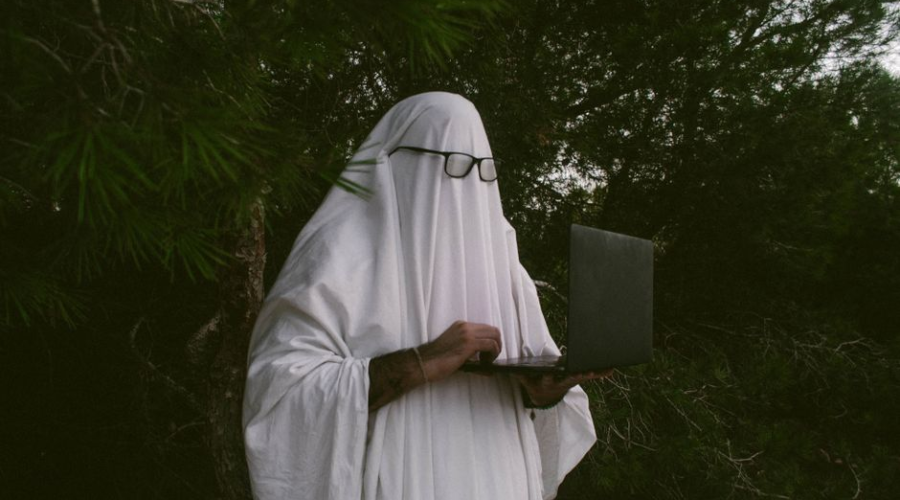 Person dressed as a ghost using a laptop outdoors in a forest