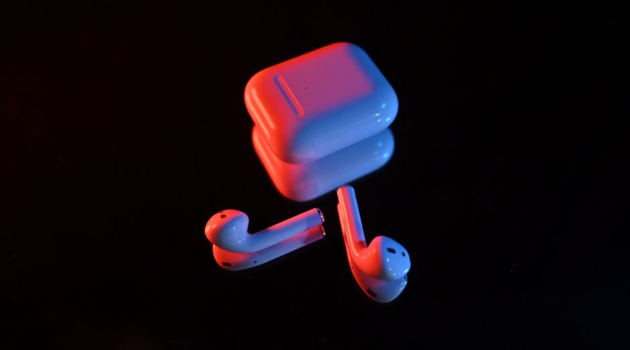 Wireless earbuds with charging case lit by blue and red light on a black background