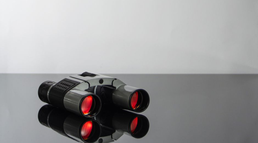 Black binoculars with red lenses on a reflective black surface