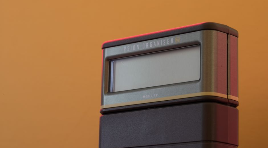 Close-up of a vintage handheld electronic device with blank screen on an orange background