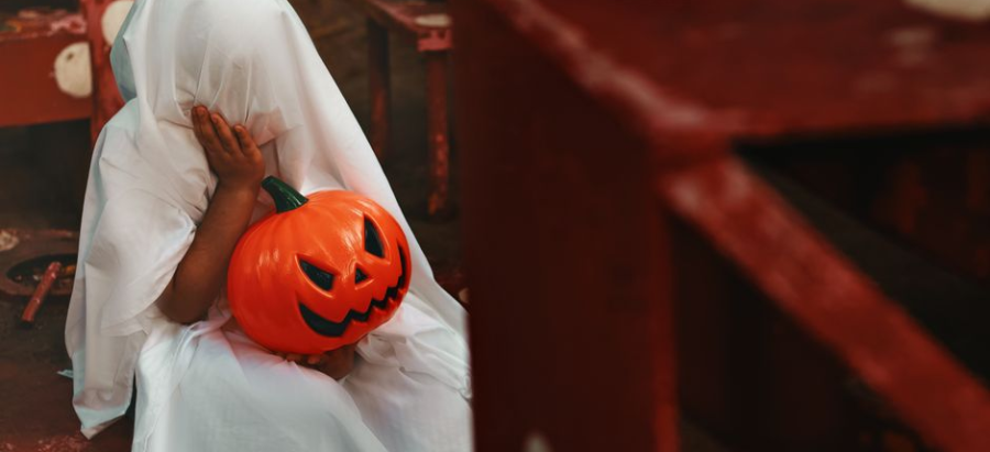 Child dressed as a ghost holding a pumpkin bucket on Halloween.