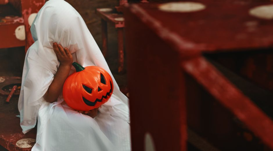 Child dressed as a ghost holding a pumpkin bucket on Halloween.