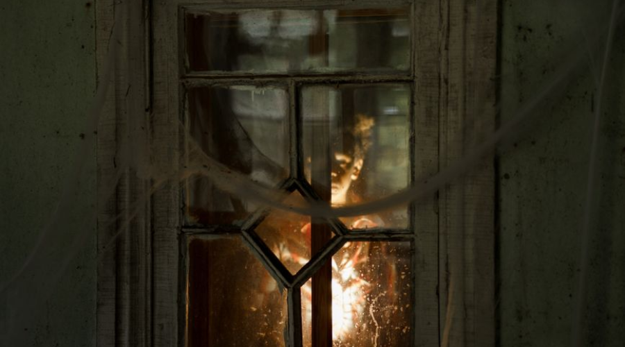 Broken-paned wooden window glowing with warm light, evoking Bannack State Park’s haunted ghost-town past