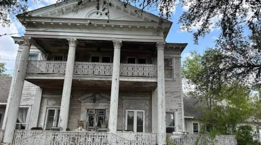 Historic abandoned mansion with classical columns and ornate ironwork railing