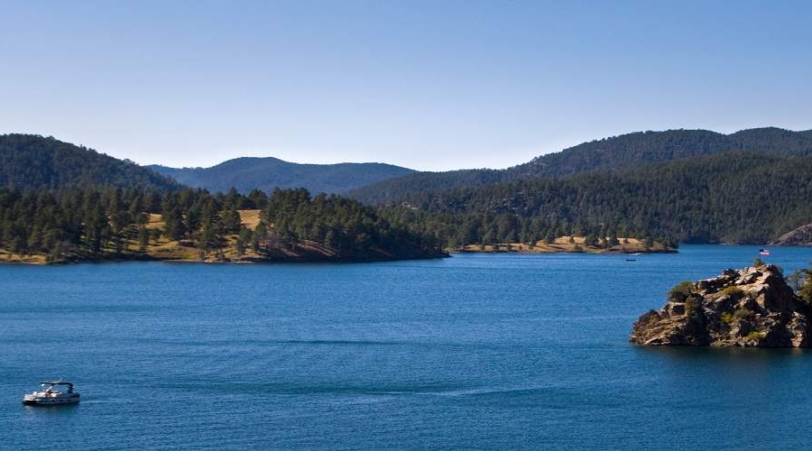 Calm lake with a boat and rocky island, surrounded by forested hills.