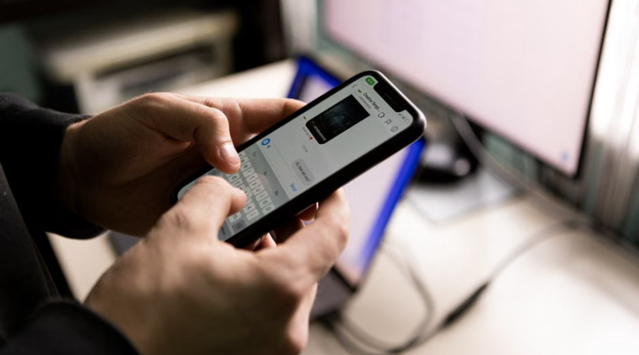 Person browsing an online store on a smartphone with a computer screen in the background