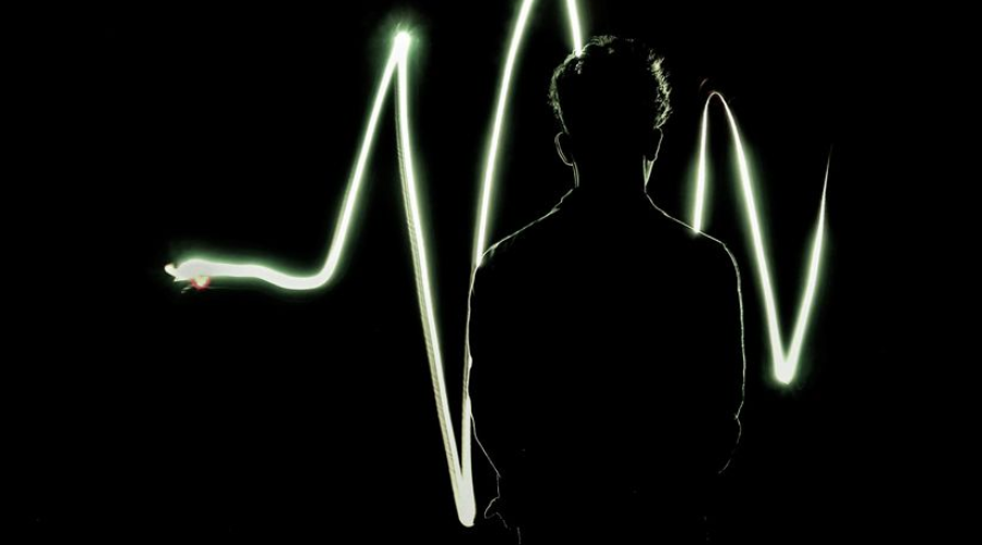 Silhouette of a person before a glowing heartbeat waveform on a black background