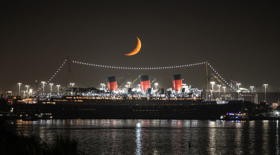 Illuminated ocean liner docked at night beneath a crescent moon