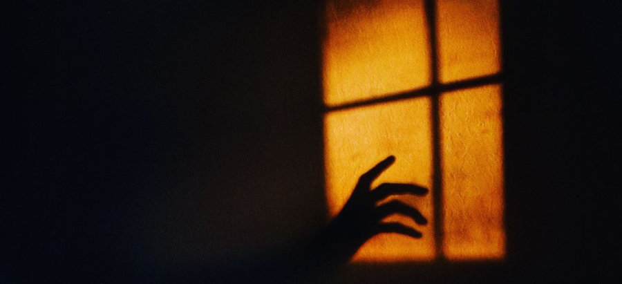 Shadow of a hand reaching toward a window in warm orange light