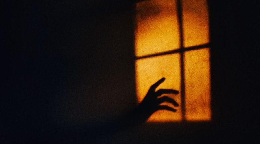 Shadow of a hand reaching toward a window in warm orange light