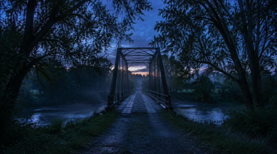 Misty old metal bridge over a river at twilight, framed by trees