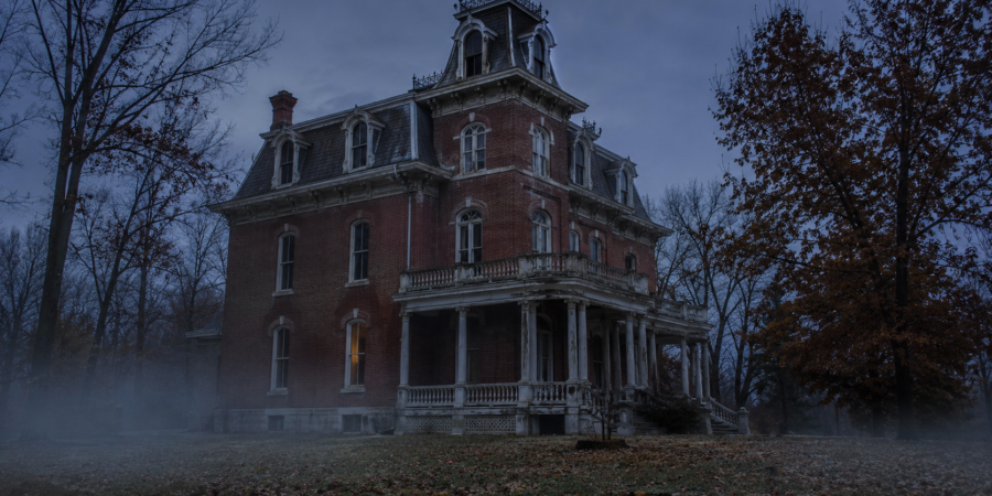 Spooky Victorian mansion in fog at dusk, framed by bare trees.