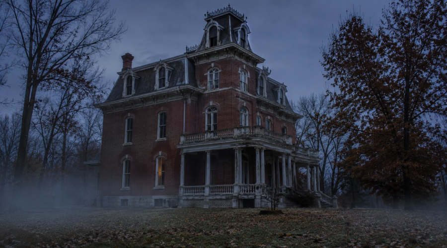 Spooky Victorian mansion in fog at dusk, framed by bare trees.