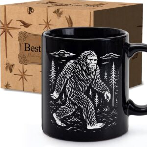 Black coffee mug with white Bigfoot silhouette, forest background, and gift box for cryptid lovers
