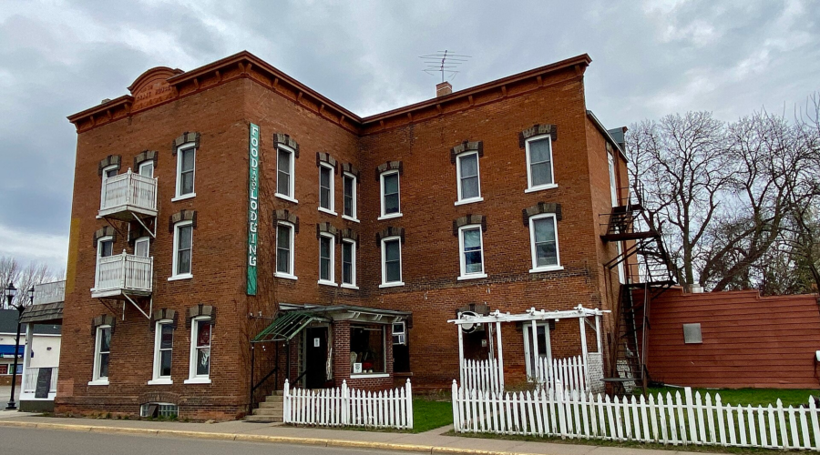 Historic three-story red-brick Grant House Hotel in Rush City, Minnesota, with balconies and a white picket fence