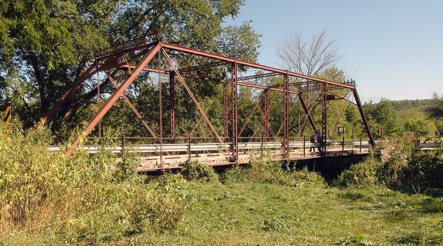 Rustic red steel truss bridge over a grassy creek, surrounded by trees in Historic Forestville