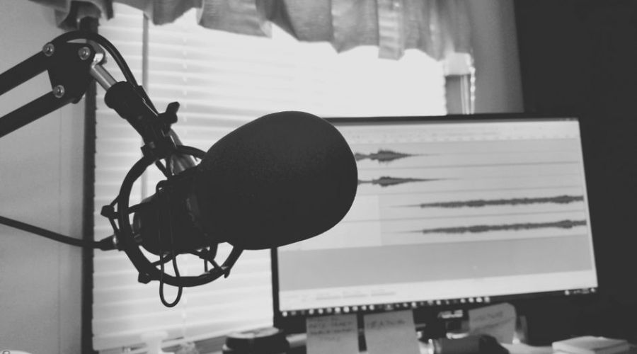 Professional podcast microphone setup with audio editing software on computer screens
