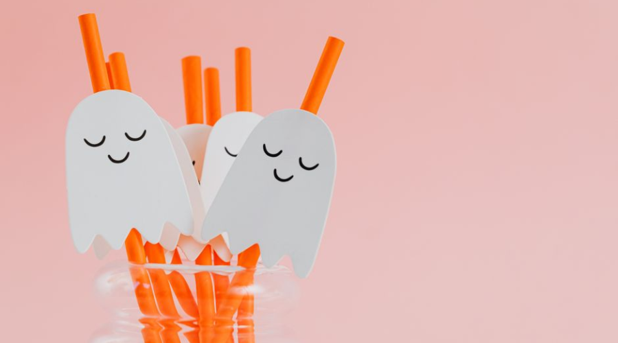 Cute ghost-themed Halloween drink stirrers in a jar on a pink background