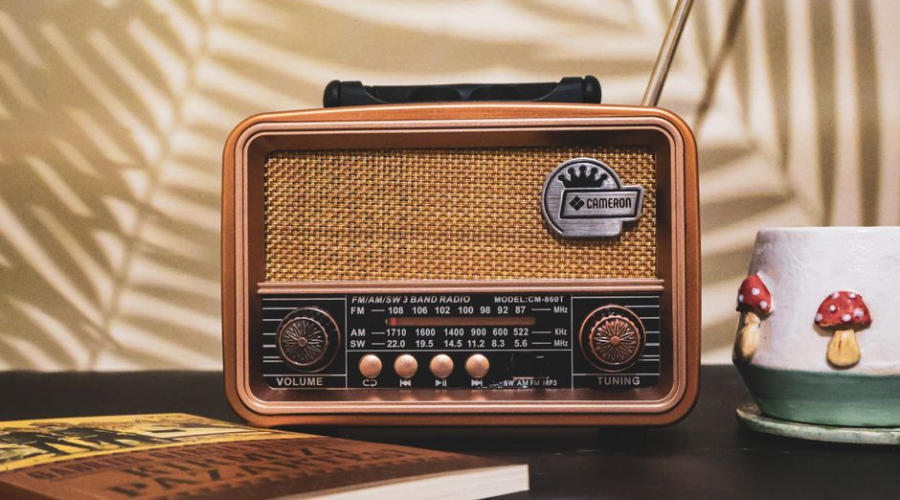 Vintage retro radio beside a snow globe and book on a dark table with warm palm-leaf shadows.