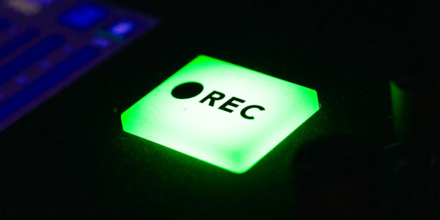 Close-up of a glowing green REC button on a recording device.