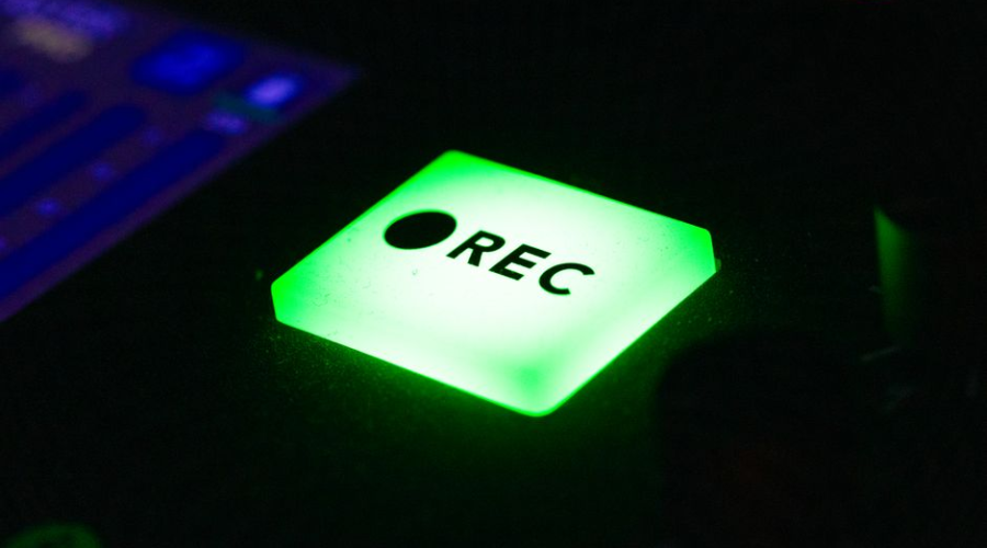 Close-up of a glowing green REC button on a recording device.