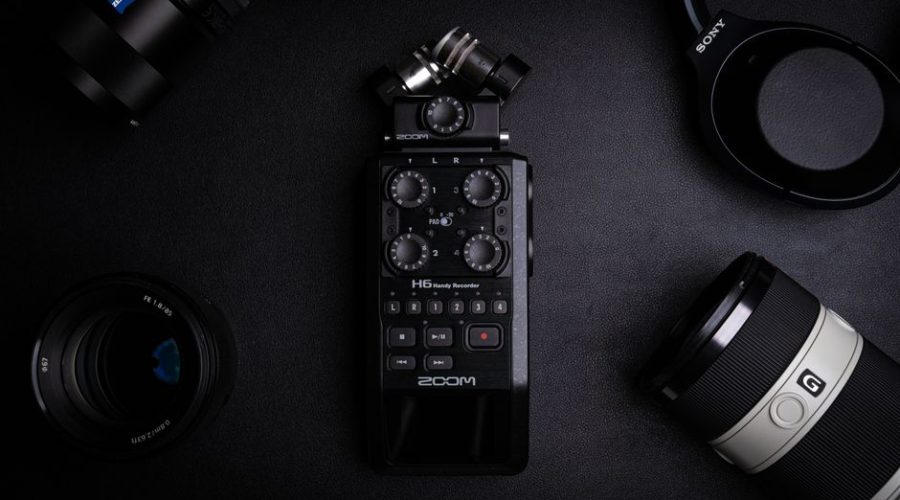 High-quality audio recorder surrounded by camera lenses and headphones on a dark surface.
