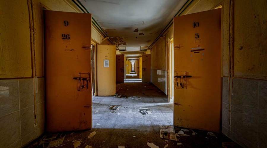 Abandoned hospital hallway with open orange doors and debris scattered across the floor