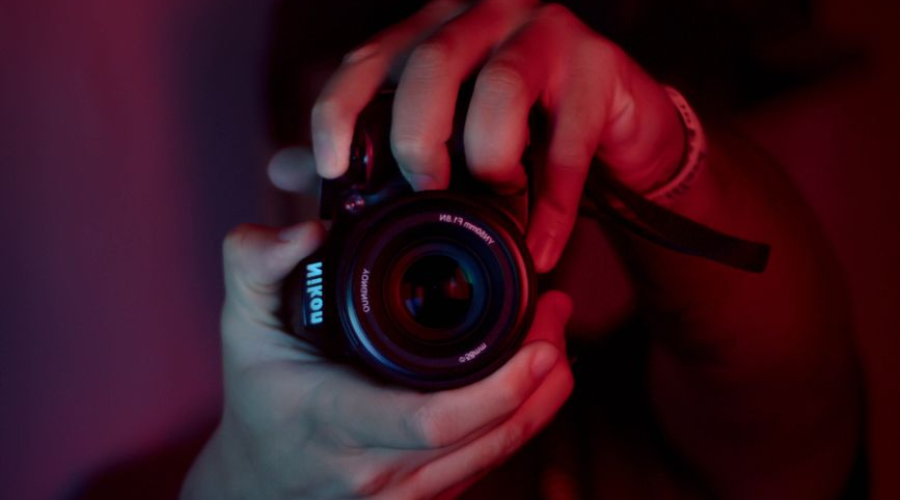 Photographer holding a camera with large lens in a moody red-lit dark studio