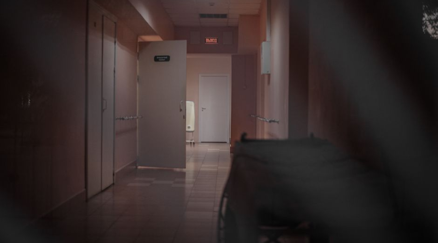 Dimly lit hospital corridor with an empty wheelchair beside an open door